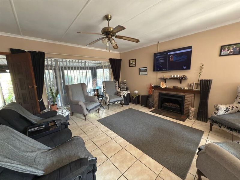 A living room featuring a brick fireplace, tiled flooring, and a ceiling fan, with direct access to an outdoor patio area.