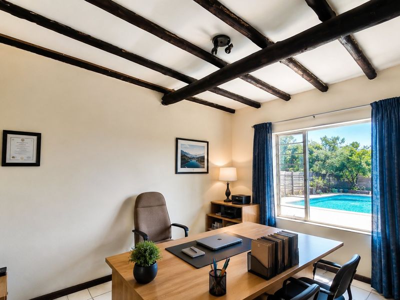 A well-lit home office featuring exposed timber ceiling beams, tiled flooring, and a large window overlooking the swimming pool area.
