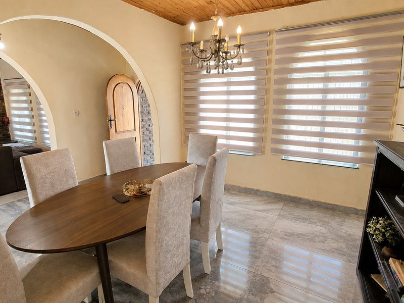 A well-lit dining room featuring an arched doorway, timber ceiling, tiled flooring, and a classic chandelier, creating a warm and inviting atmosphere.