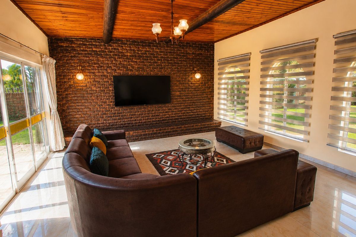 Spacious living room featuring an exposed timber beam ceiling, a striking exposed brick feature wall with built-in media console, and large sliding doors to garden.