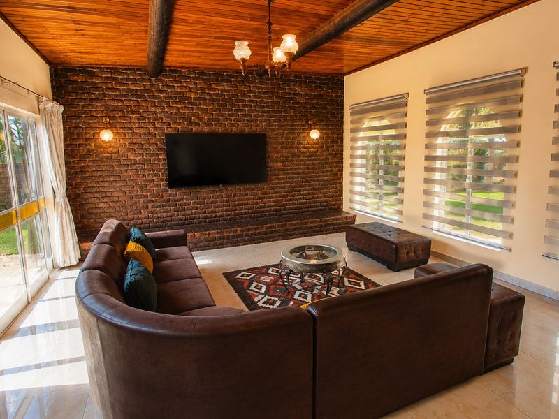Spacious living room featuring an exposed timber beam ceiling, a striking exposed brick feature wall with built-in media console, and large sliding doors to garden.