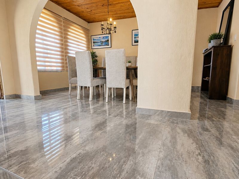 A bright dining area featuring polished grey porcelain floor tiles, a warm timber ceiling, and an elegant arched entryway leading to the exterior.