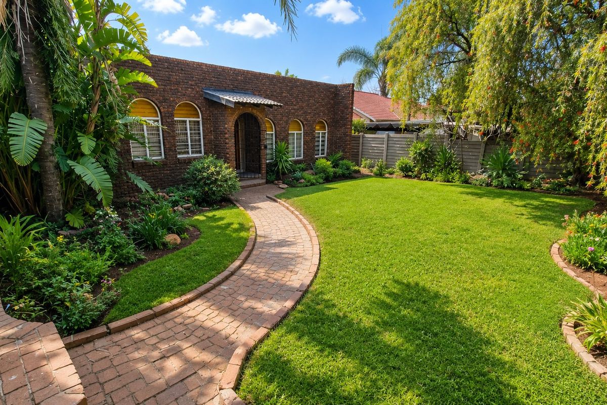 A well-maintained rear garden featuring a brick-paved pathway leading to a charming brick facade with arched windows and lush landscaping.