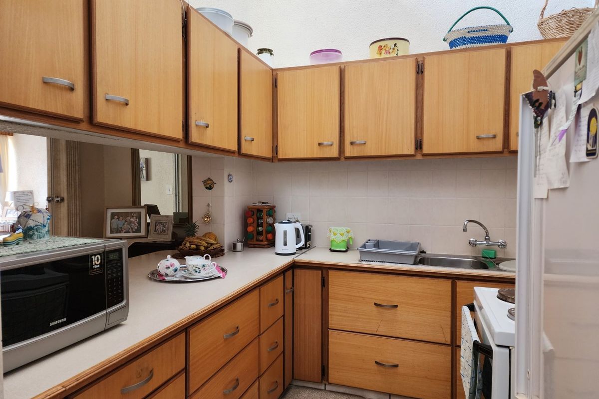 A functional kitchen featuring dated wooden cabinetry, laminate countertops, a tiled backsplash, and a stainless steel sink.