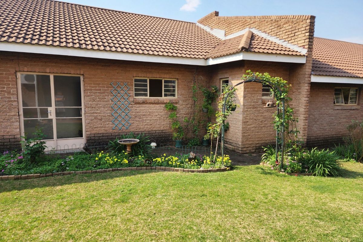 Rear view of the apartment featuring a face brick facade, tiled roof, and a well-maintained garden area with a metal archway.