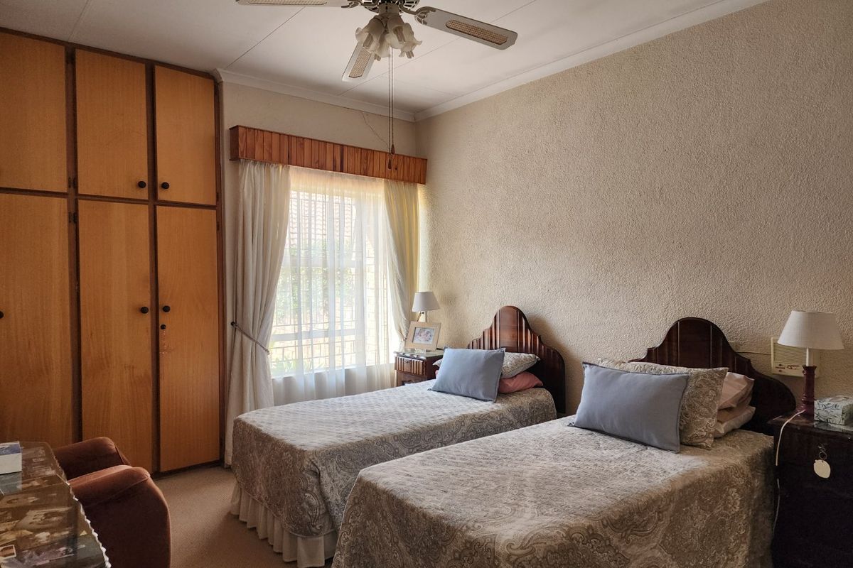 A bedroom featuring built-in wooden cupboards, a ceiling fan, and textured wall finishes, offering a functional space with classic design elements.