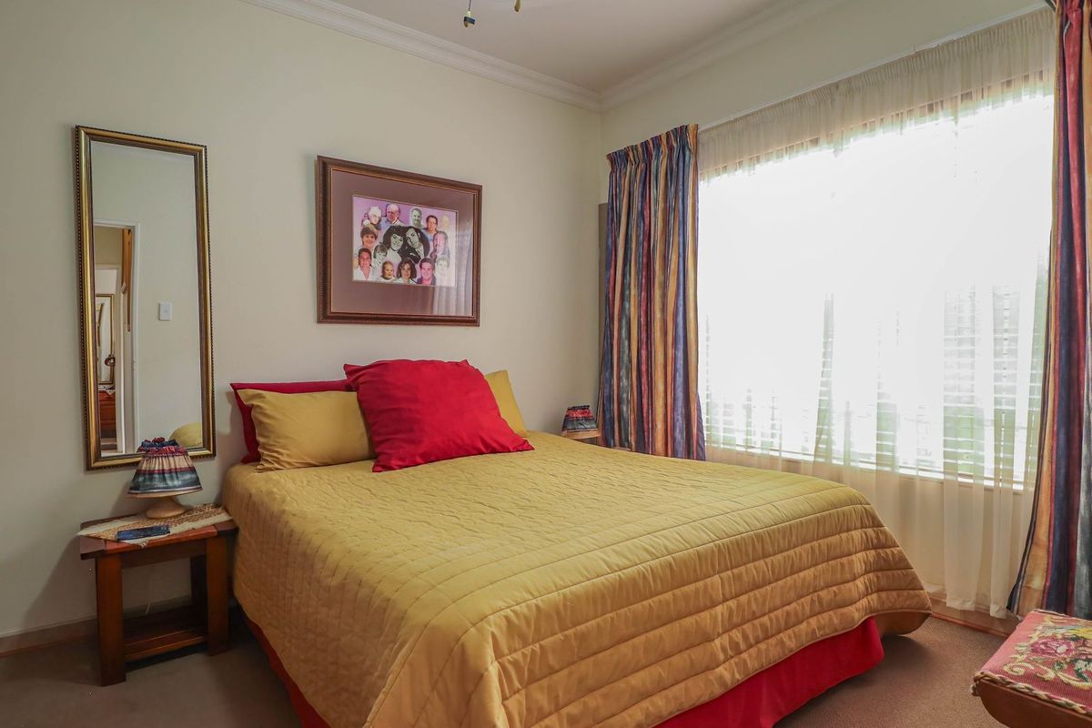 A well-lit bedroom featuring neutral wall finishes, carpeted flooring, and a large window with curtain tracks.