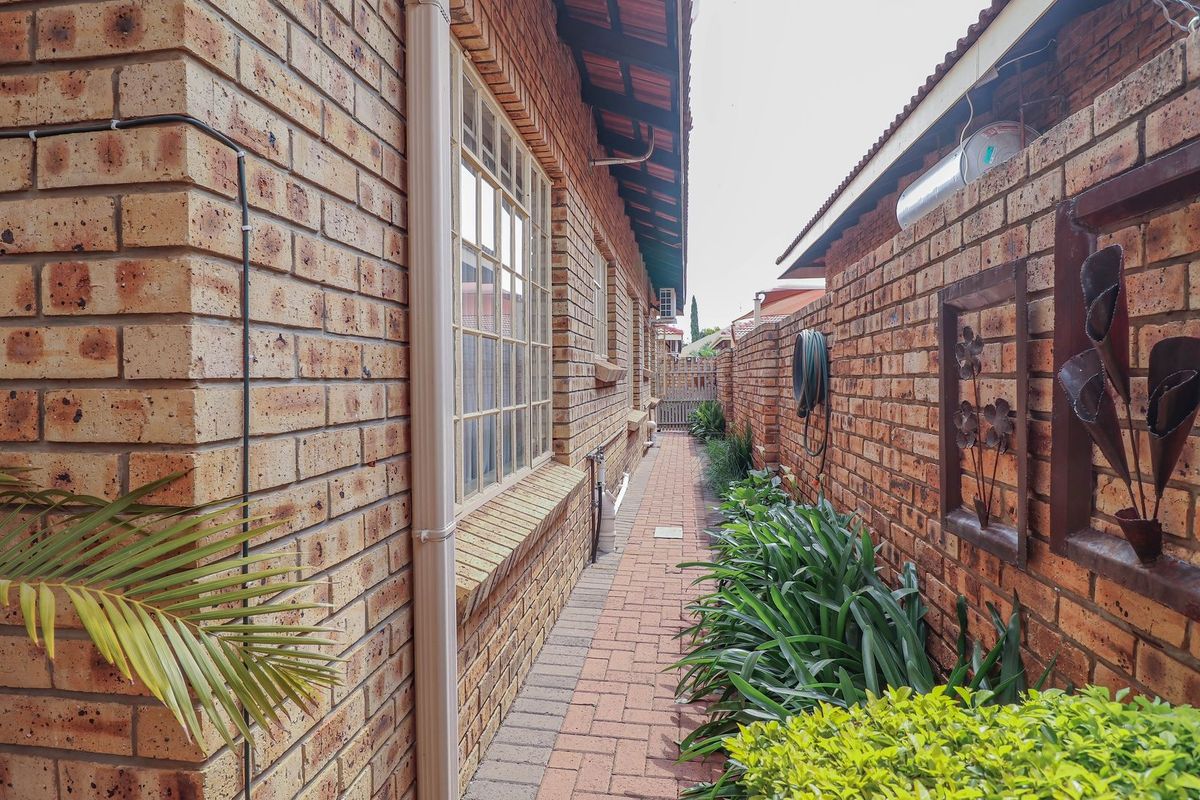 A narrow side walkway featuring face brick walls, paved flooring, and a gutter downpipe, providing access along the side of the townhouse.