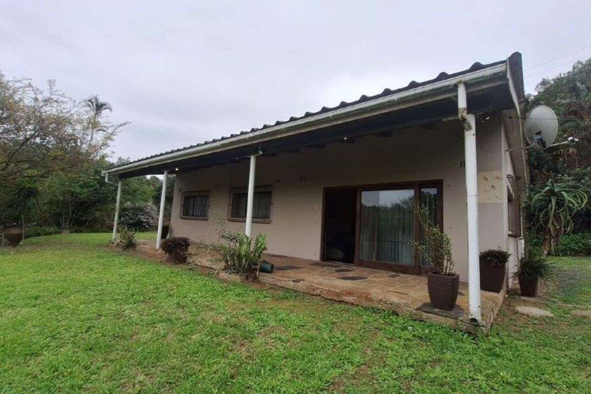 Rear view of the house featuring a covered patio with stone paving, sliding glass doors, and surrounding garden space.