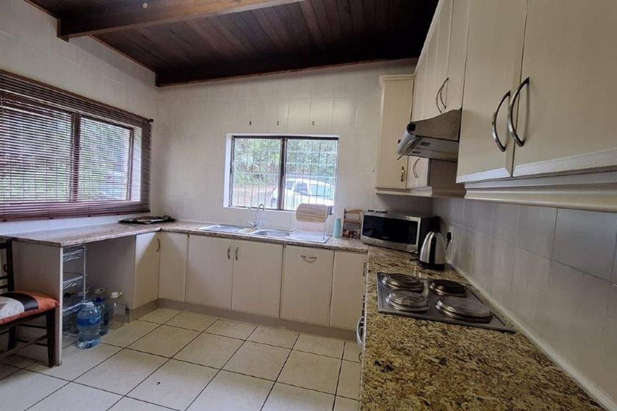 Functional kitchen featuring granite countertops, built-in cabinetry, electric hob, extractor fan, and exposed timber ceiling beams.