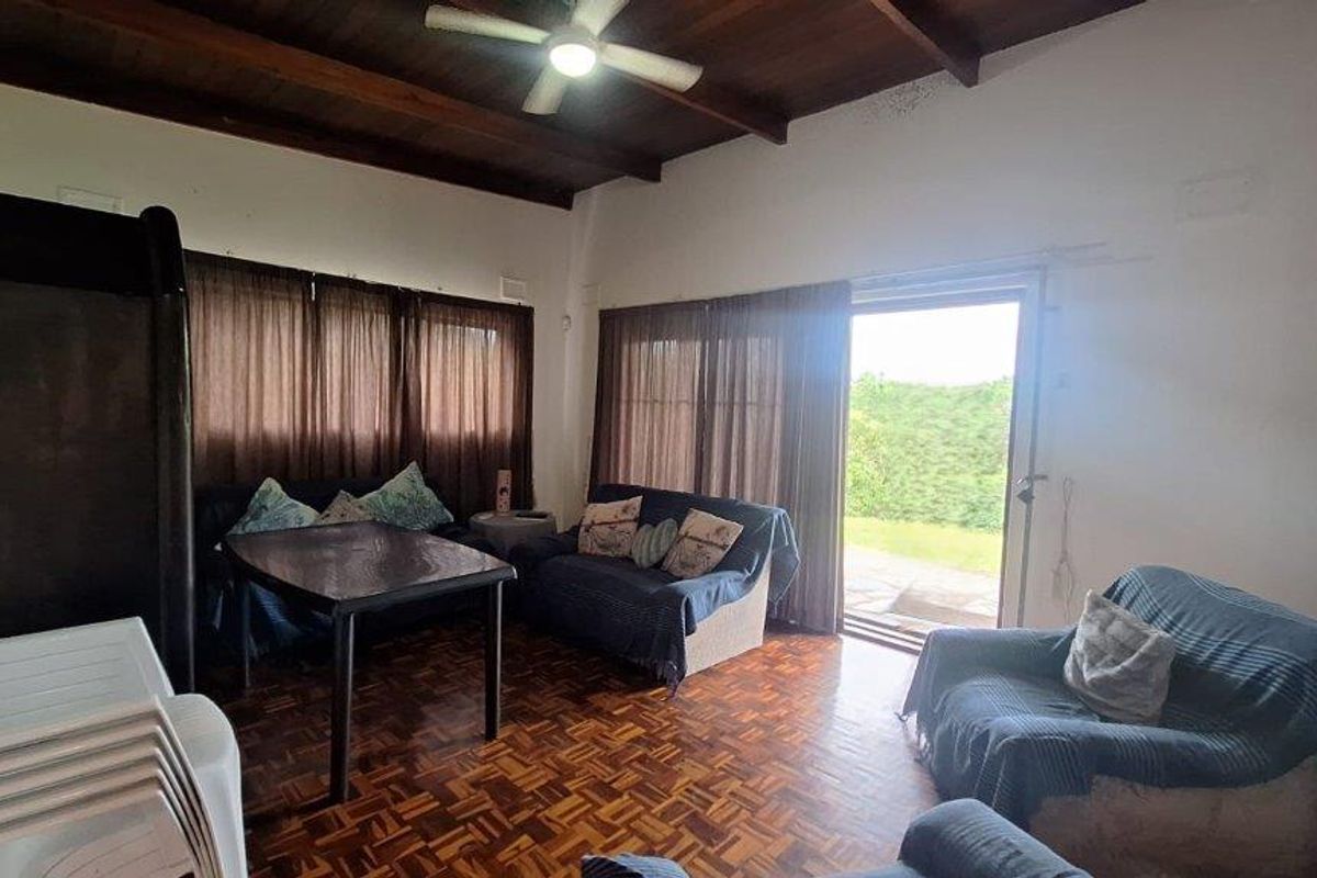 Living room featuring exposed timber beam ceilings, parquet flooring, and a sliding glass door providing access to the outdoor area.