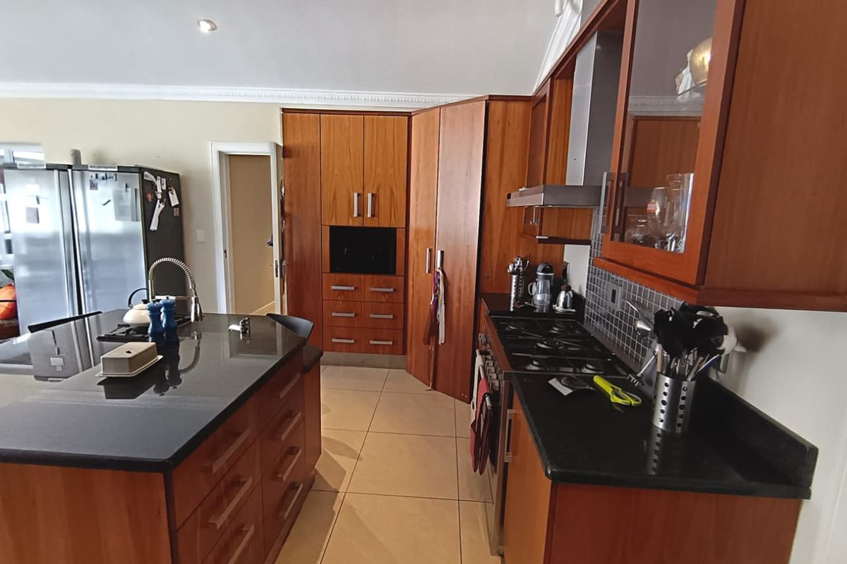 A functional kitchen featuring warm-toned wooden cabinetry, granite countertops, a central island, and a gas hob with an integrated extractor fan.
