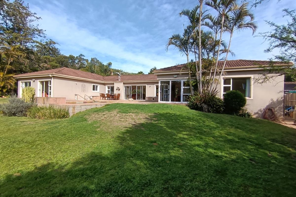 Rear view of the house featuring a spacious lawn, paved patio area, and multiple sliding glass door access points to the interior living spaces.