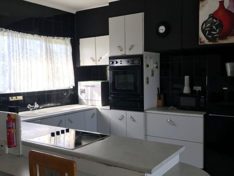 A functional kitchen featuring built-in oven, electric cooktop, double sink, and contrasting black and white cabinetry with tiled backsplash.