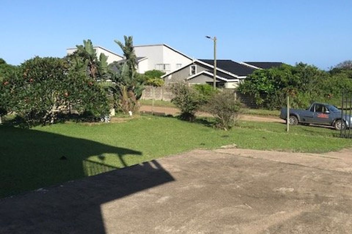 A view of the rear yard featuring a concrete driveway and lawn area, with surrounding boundary walls and neighbouring properties visible.