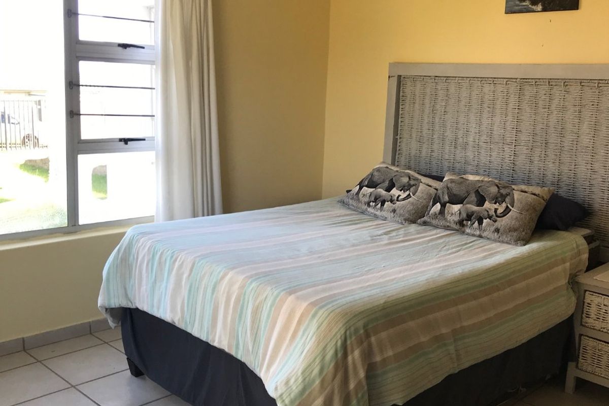 A functional bedroom featuring tiled flooring and a large window with security bars, providing natural light and a view of the exterior.
