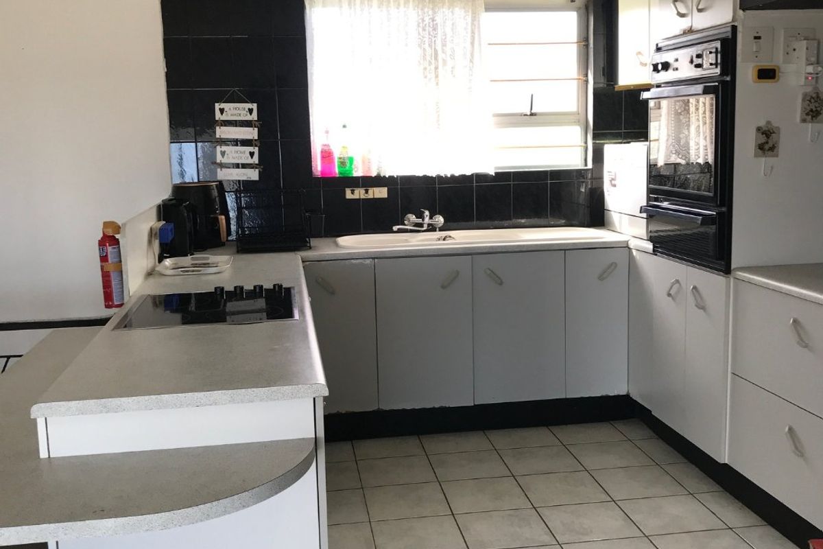 Functional kitchen featuring built-in cabinetry, laminate countertops, a built-in oven, electric hob, and ceramic tile flooring with a black tiled backsplash.