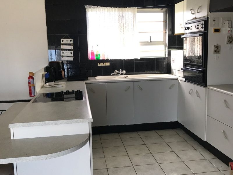 Functional kitchen featuring built-in cabinetry, laminate countertops, a built-in oven, electric hob, and ceramic tile flooring with a black tiled backsplash.