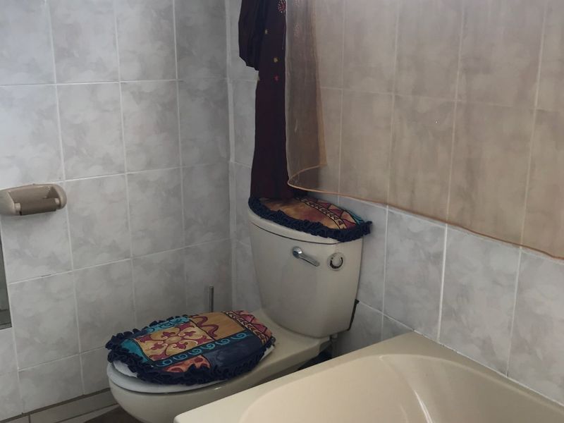 A functional bathroom featuring a standard bathtub, toilet, and full-height wall tiling. The space is dated and would benefit from modern updates.
