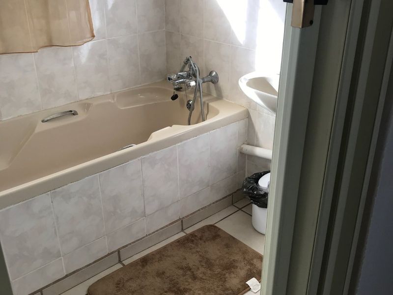 A compact bathroom featuring a beige bathtub with wall-mounted faucet, pedestal sink, and neutral ceramic wall and floor tiling.