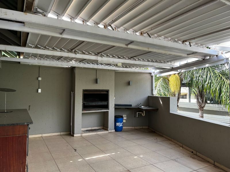 Covered outdoor patio featuring a built-in braai, sink, stone countertop, and louvered roof, providing a functional space for outdoor entertaining.