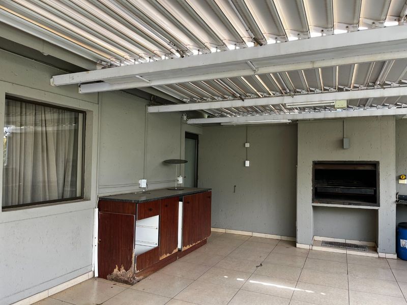 Covered outdoor patio area featuring a built-in braai, tiled flooring, and fixed cabinetry with louvered roof structure.