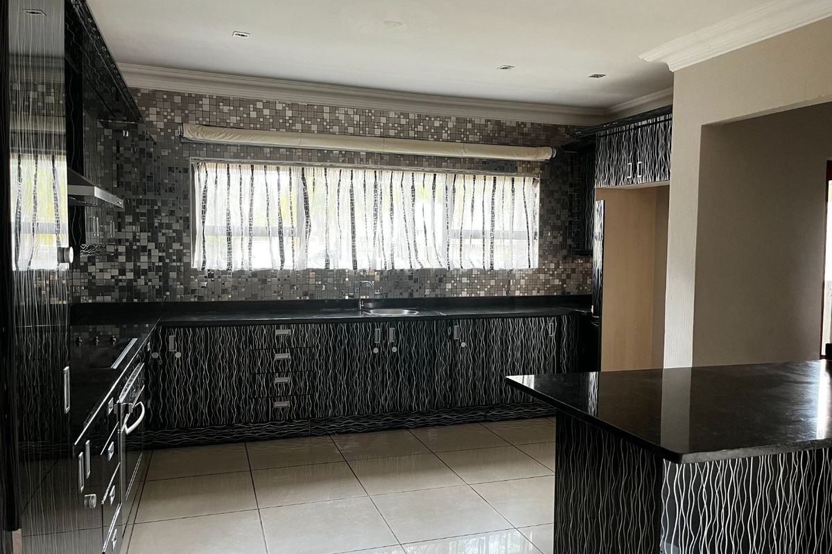 Spacious kitchen featuring modern patterned cabinetry, granite countertops, a central island, and a decorative mosaic tile backsplash with integrated appliances.