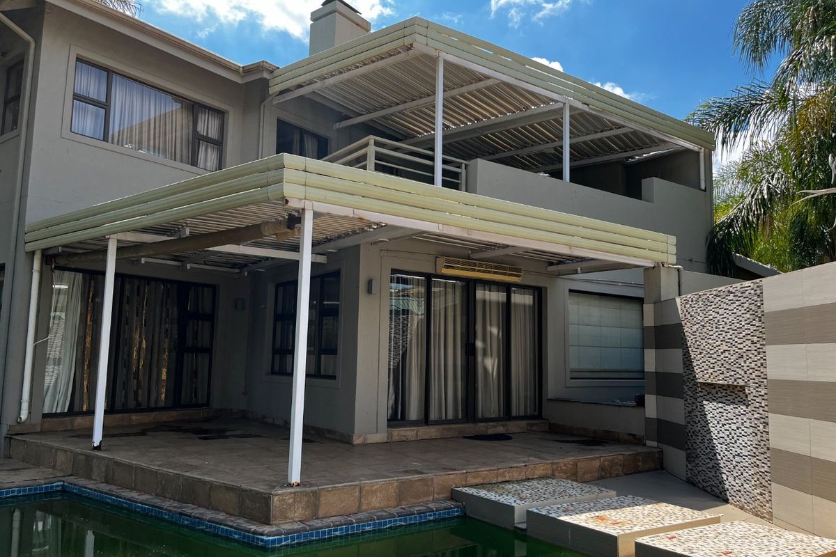 Rear exterior view featuring a swimming pool, covered patio area, upper balcony, and a decorative mosaic feature wall.