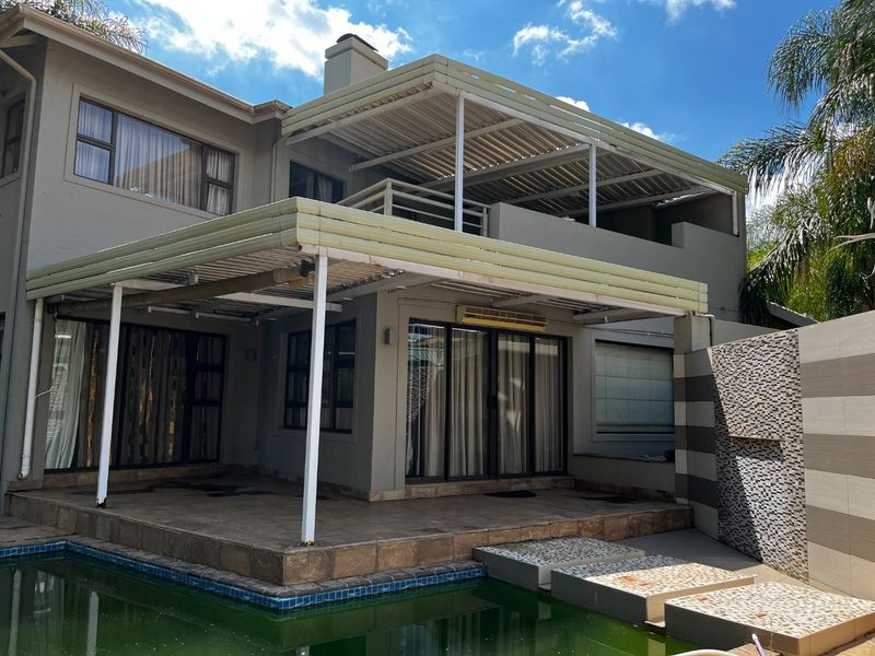 Rear exterior view featuring a swimming pool, covered patio area, upper balcony, and a decorative mosaic feature wall.