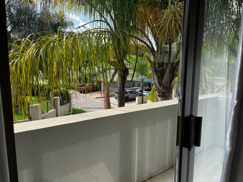 A view from a balcony featuring a solid concrete balustrade and tiled flooring, overlooking a residential street and garden area.