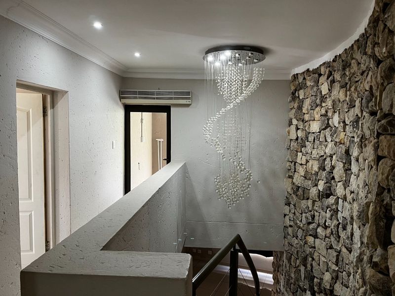 A well-lit hallway featuring a striking stone accent wall, a modern crystal chandelier, and a clean, minimalist aesthetic with a wall-mounted air conditioning unit.