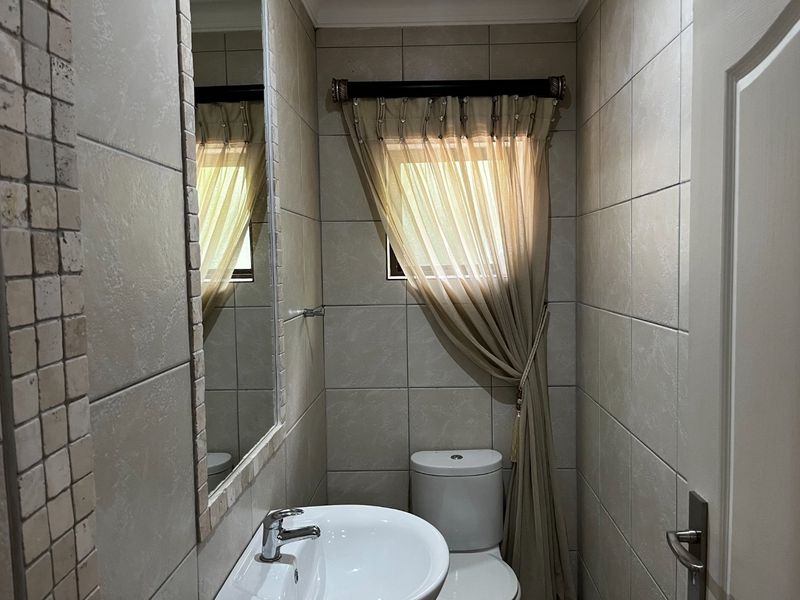 A compact guest bathroom featuring neutral ceramic wall tiles, a pedestal basin with chrome mixer, and a flush toilet.