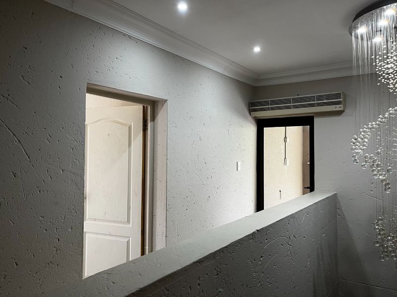A well-lit hallway featuring textured walls, crown molding, and a wall-mounted air conditioning unit.