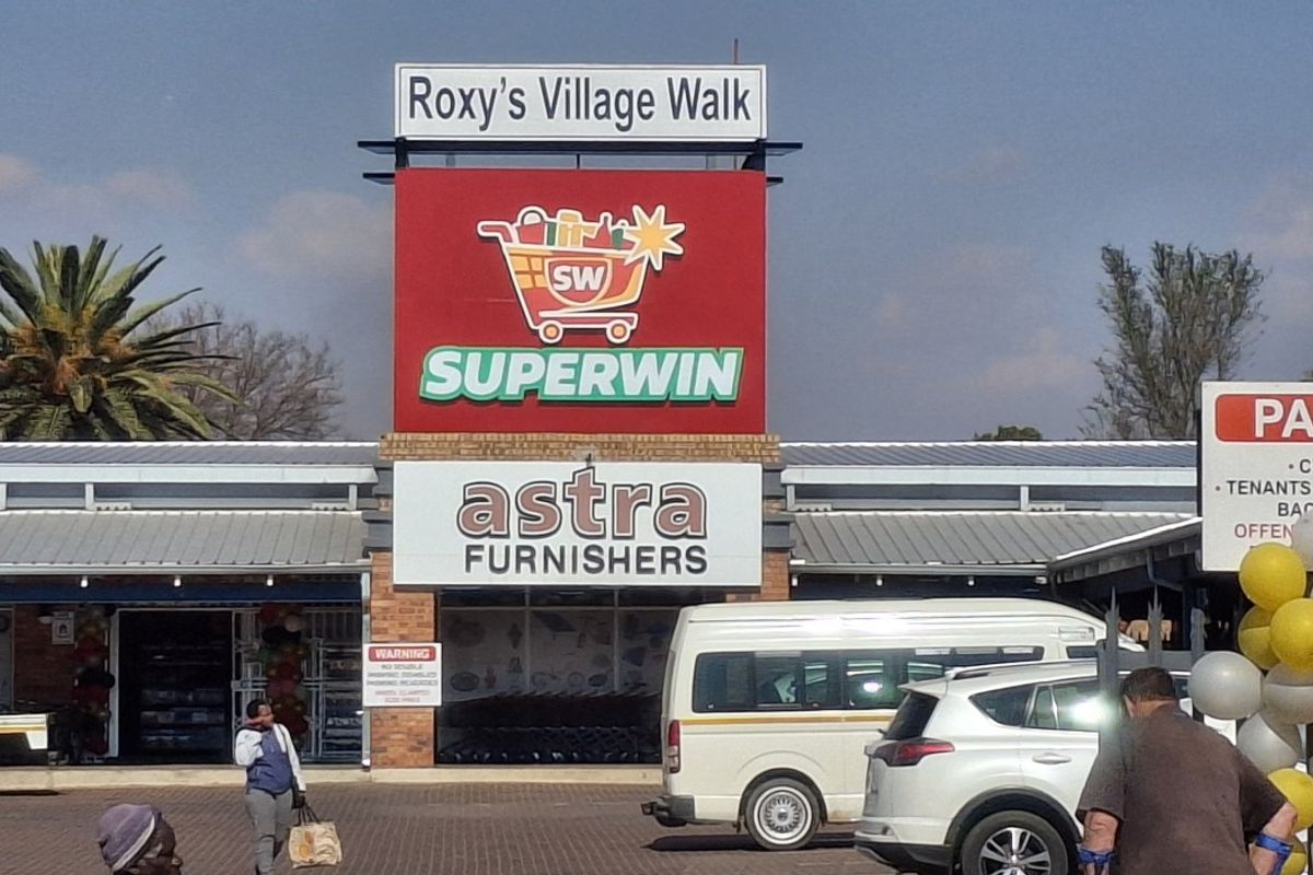 Front exterior view of Roxy's Village Walk commercial center featuring prominent signage for Superwin and Astra Furnishers with an adjacent paved parking area.