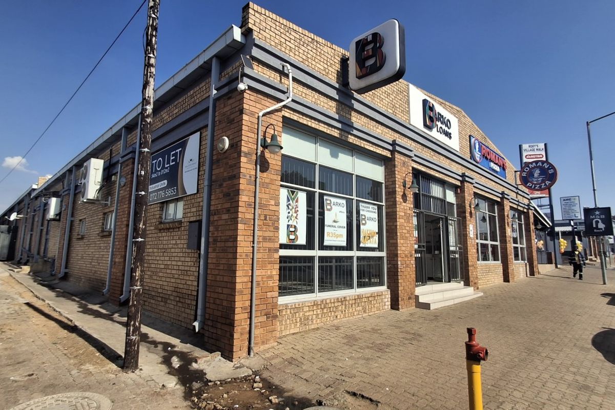 Front exterior view of a commercial retail building featuring brick construction, large display windows, and prominent signage along a paved street.