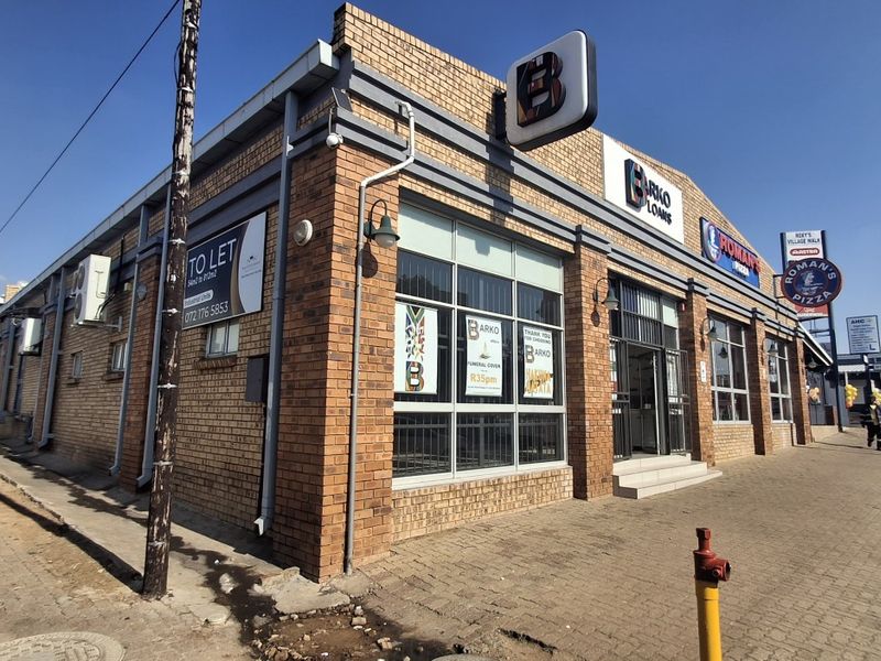 Front exterior view of a commercial retail building featuring brick construction, large display windows, and prominent signage along a paved street.