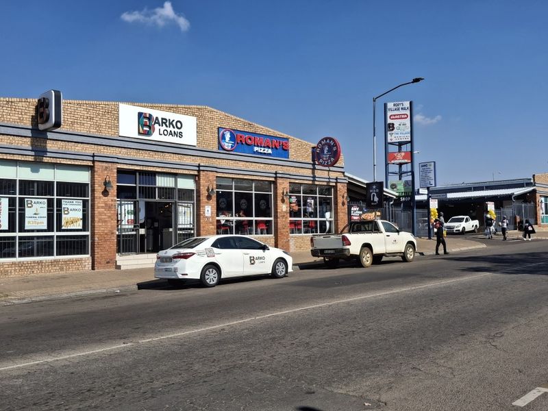 Street-level view of a commercial retail strip center featuring face brick construction, large display windows, and prominent tenant signage.