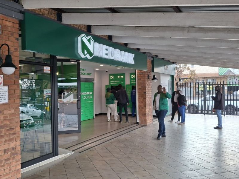 A commercial bank storefront featuring a covered walkway, brick facade, and integrated ATM service area with glass entrance doors.