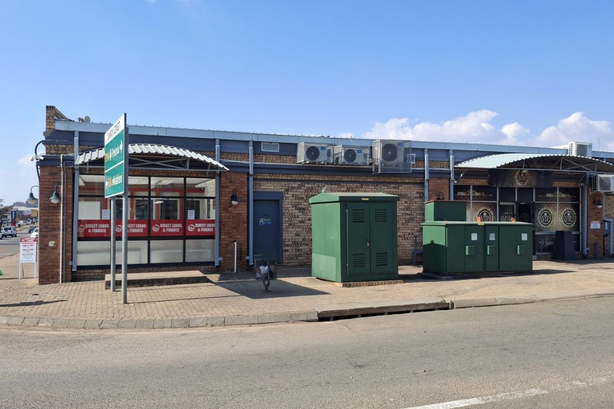 Street-level view of a commercial property featuring a brick facade, large storefront windows, metal awnings, and external utility infrastructure.