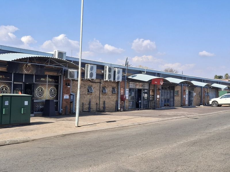 Front exterior view of a commercial strip mall featuring brick facade, multiple storefront entrances with metal awnings, and wall-mounted air conditioning units.