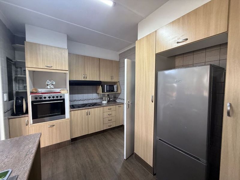 Functional kitchen featuring light wood-finish cabinetry, built-in oven and hob, tiled backsplash, and durable vinyl flooring.
