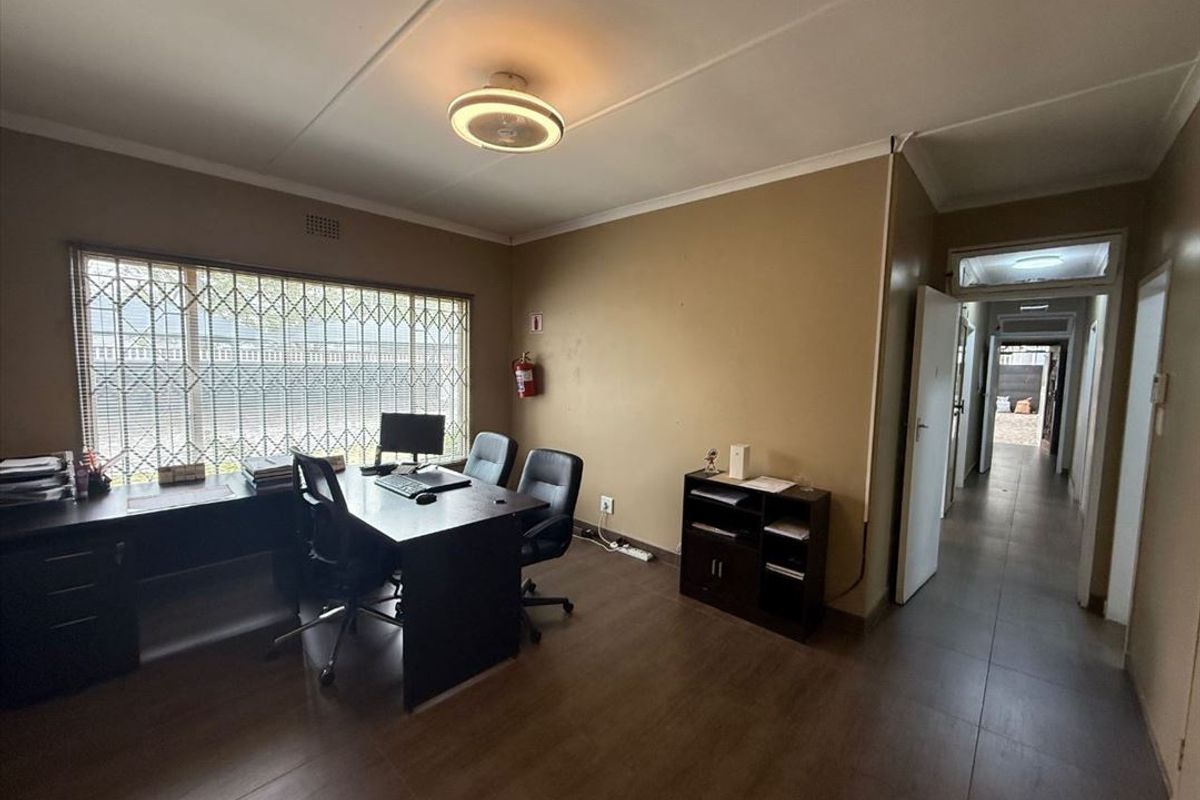 A functional office space featuring tiled flooring, security bars on the window, and direct access to the hallway.