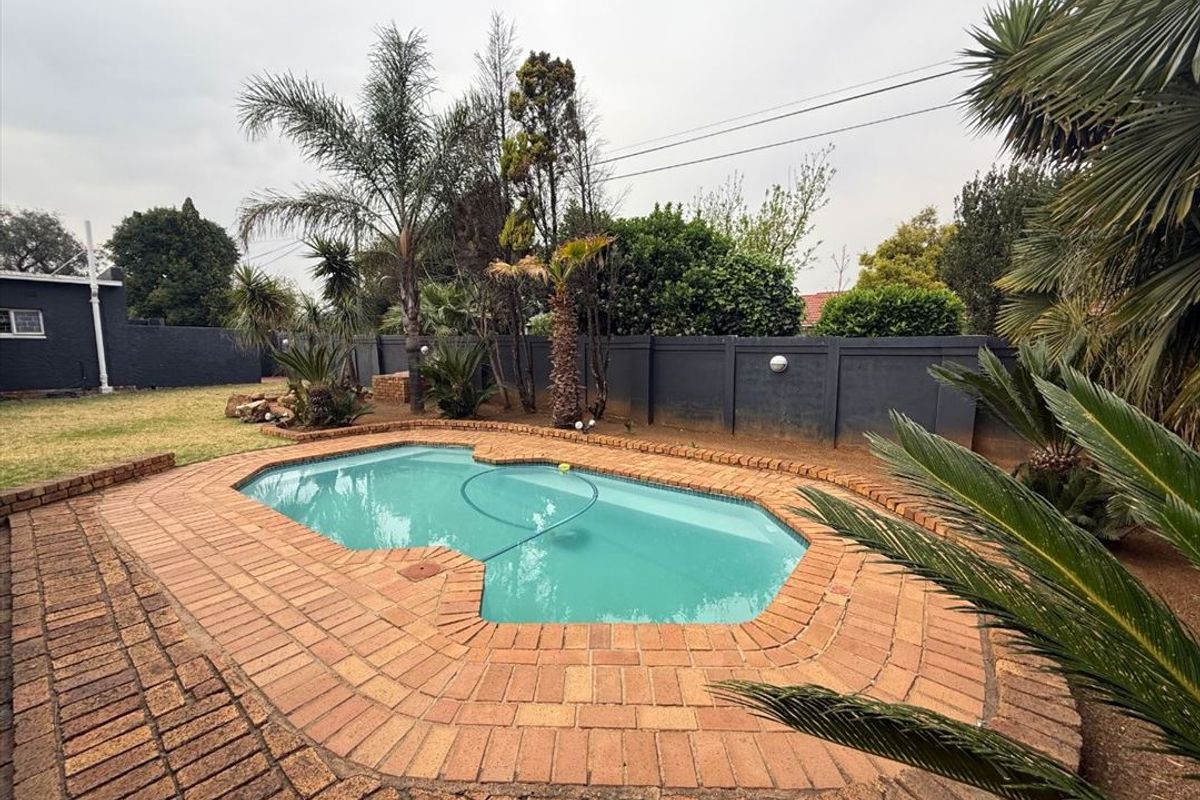 A private outdoor swimming pool area featuring brick coping, surrounded by a landscaped garden and a solid perimeter boundary wall.