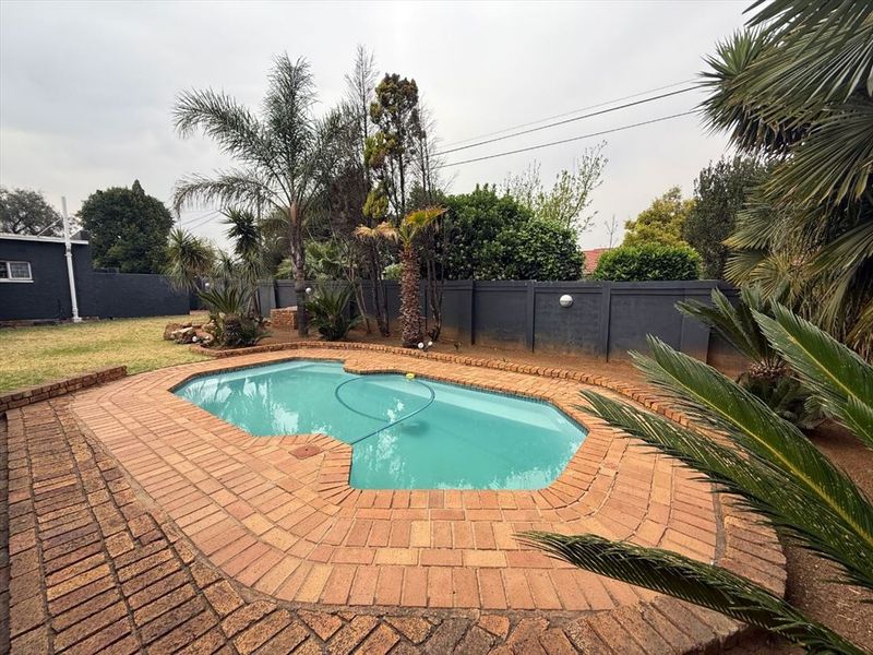 A private outdoor swimming pool area featuring brick coping, surrounded by a landscaped garden and a solid perimeter boundary wall.