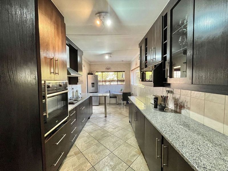 A well-maintained galley-style kitchen featuring dark wood cabinetry, granite countertops, built-in oven, and tiled flooring with an integrated dining area.