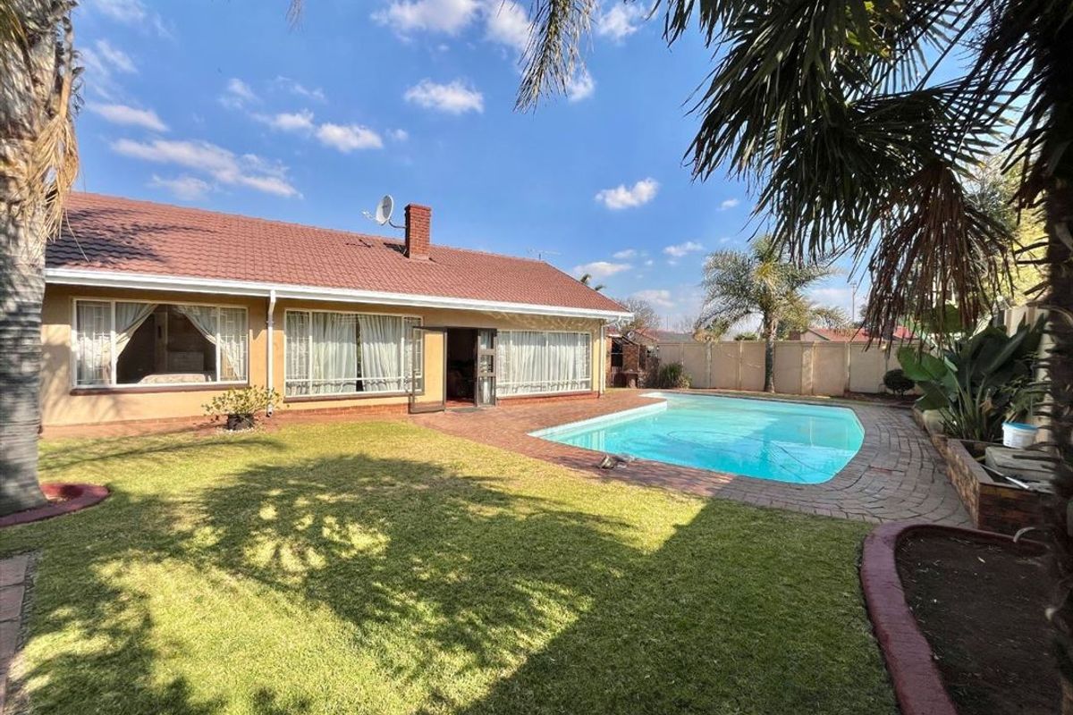 Rear view of the property featuring a swimming pool, paved surround, landscaped lawn, and a tiled roof house structure.