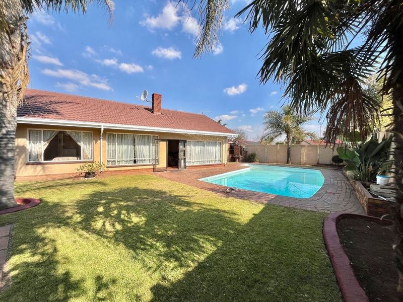 Rear view of the property featuring a swimming pool, paved surround, landscaped lawn, and a tiled roof house structure.