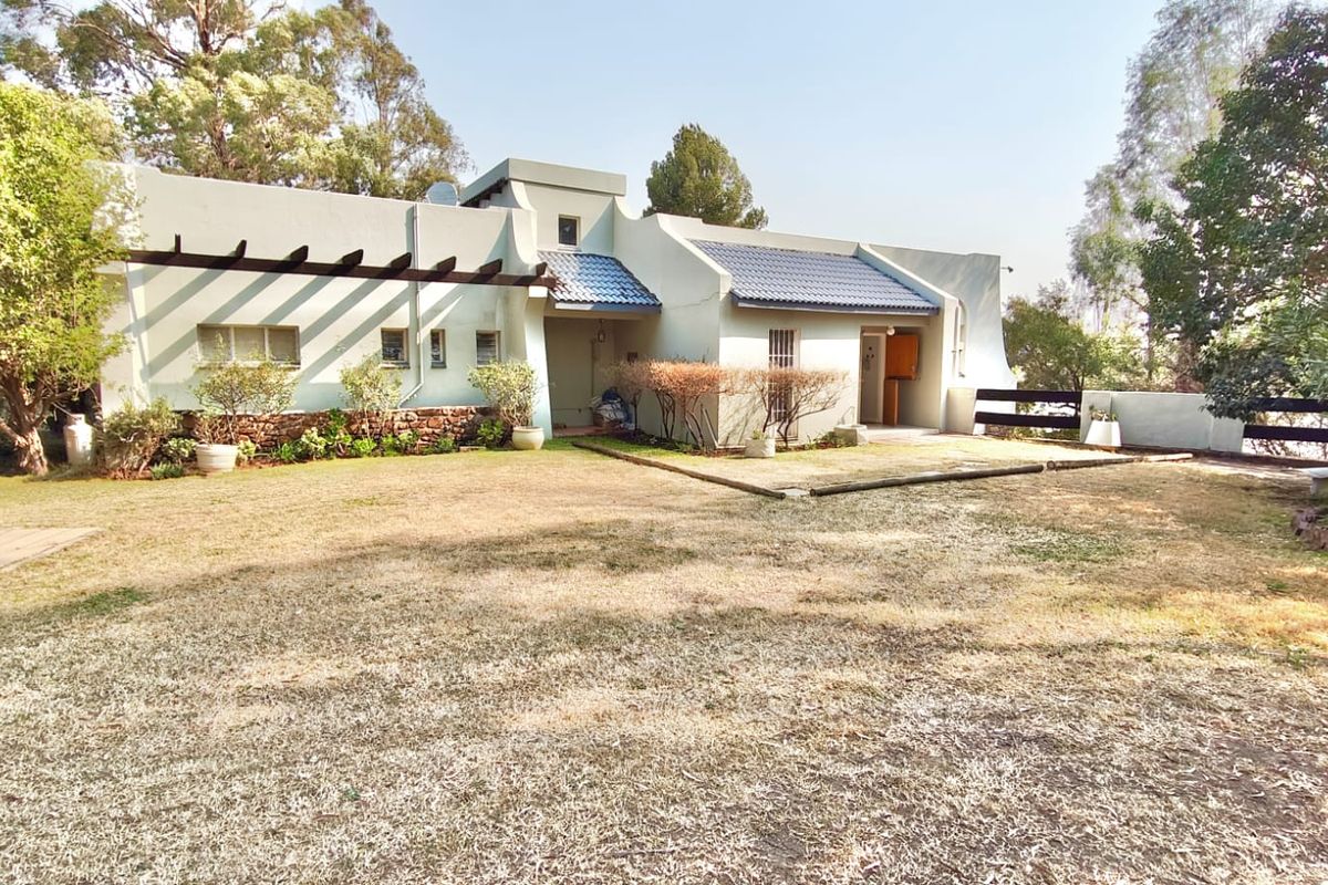 Rear view of the property featuring a tiled roof, timber pergola, and stone cladding accents, set against a large garden area.