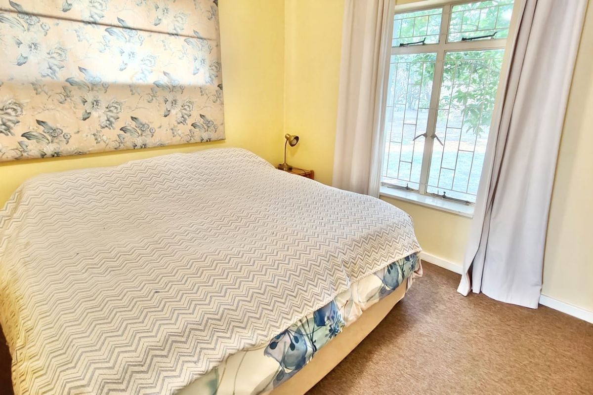 A bedroom featuring carpet flooring and a window with security bars, offering a functional space with potential for modern updates.