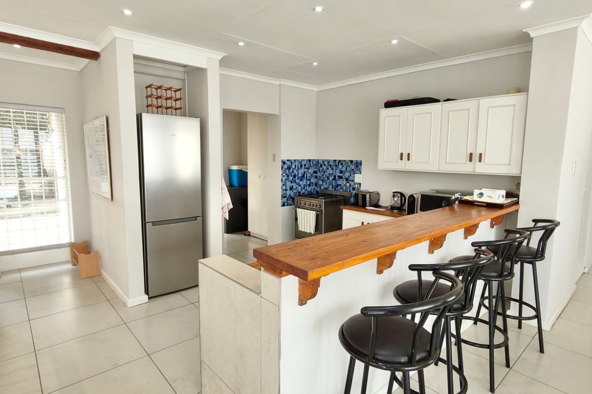 A functional kitchen featuring white cabinetry, a wooden breakfast bar, tiled splashback, and tiled flooring, with an adjacent scullery area.
